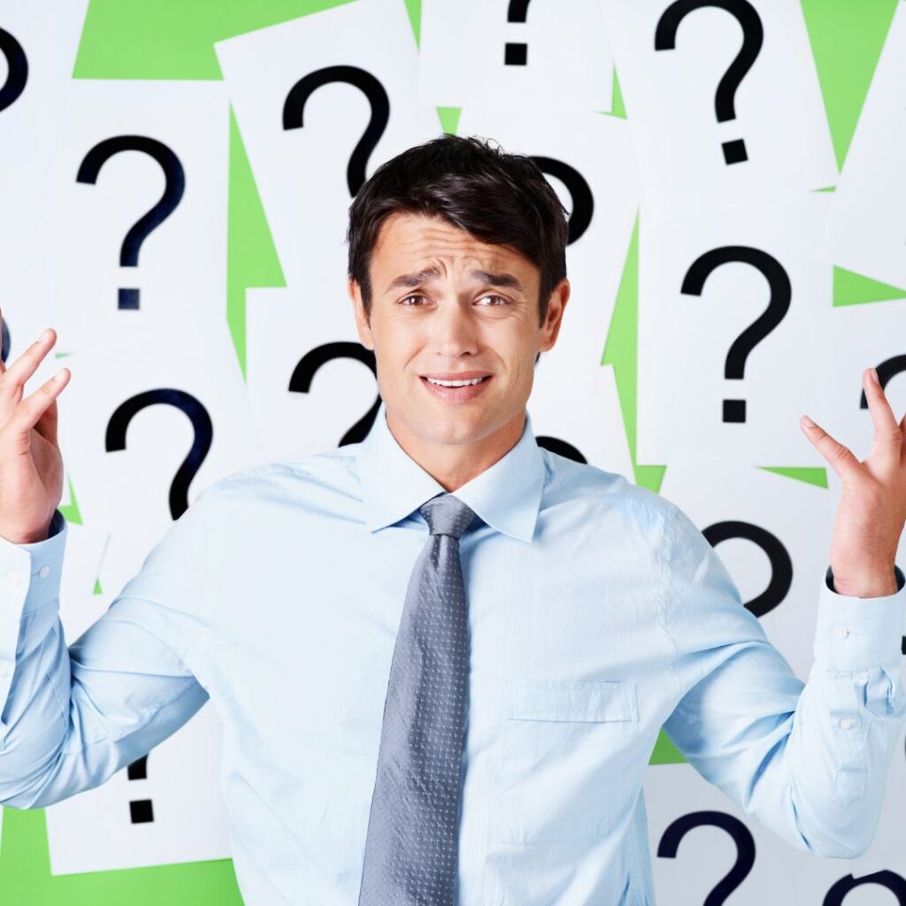 Mann im Büro mit fragendem Gesichtsausdruck vor Fragezeichen – Symbolbild für Unsicherheit bei Verantwortung und Vorschriften.
